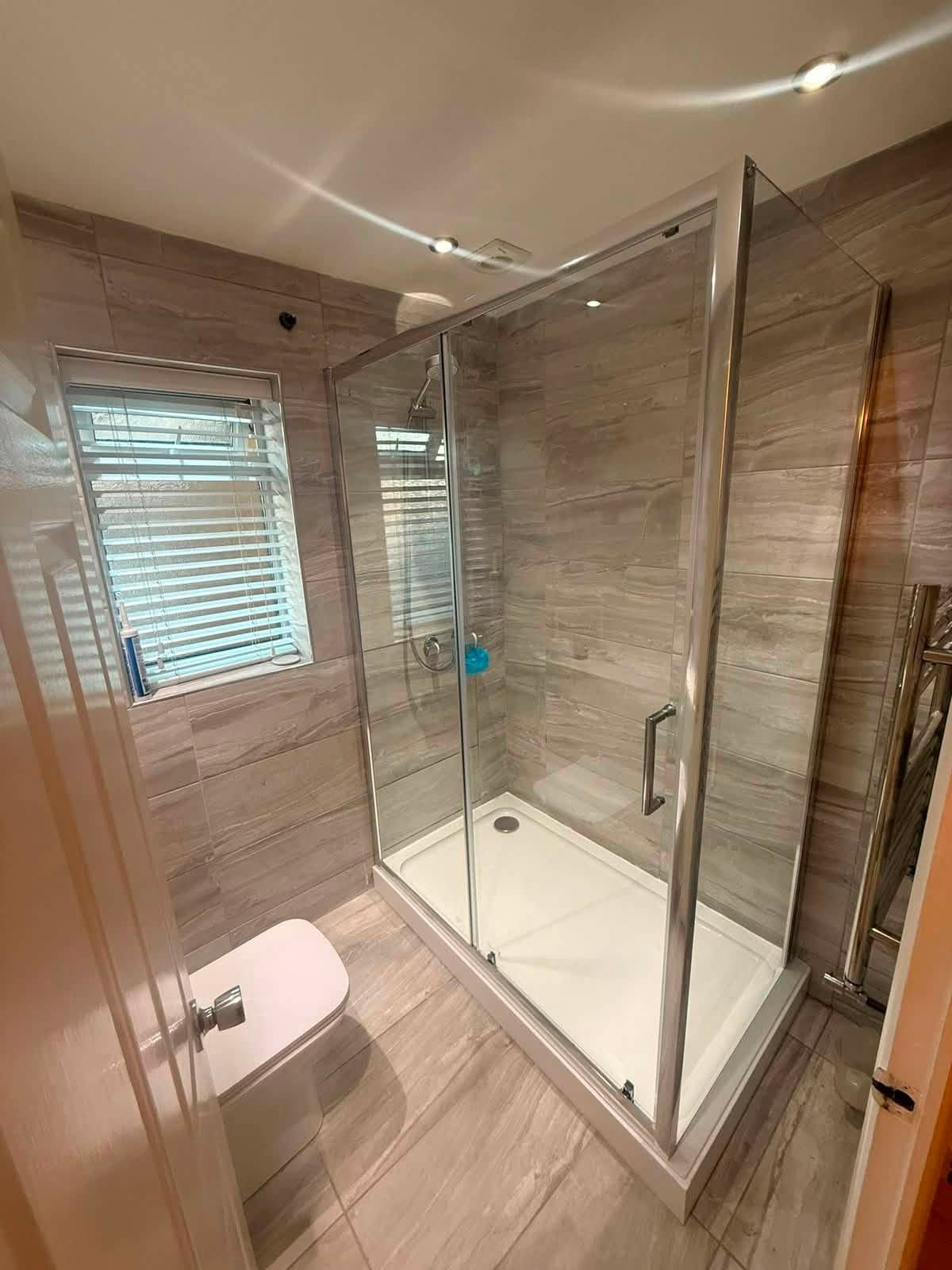 Completed bathroom with large glass shower enclosure and grey wall tiling